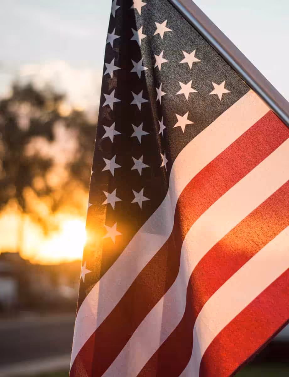 American flag waving at sunset with warm light and clear sky.